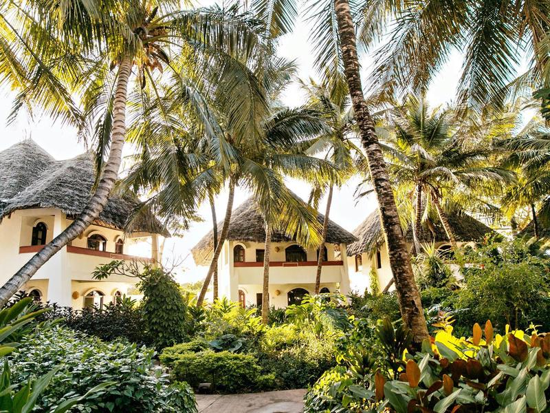 Bungalows d'hôtel avec toits de chaume entourés de palmiers et plantes tropicales