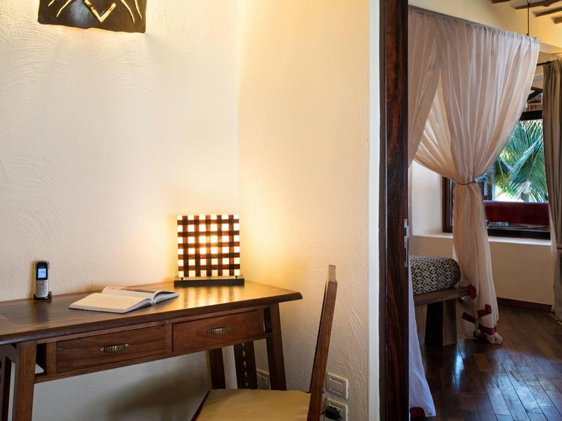 Bureau avec chaise et lampe à côté d'une pièce ouverte avec rideaux et vue extérieure.