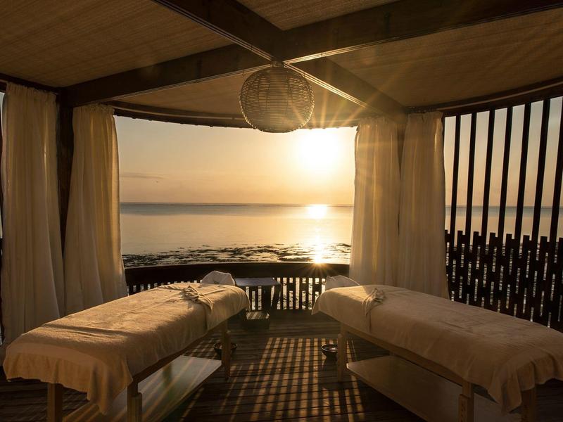 Une zone spa paisible avec deux tables de massage au coucher du soleil au bord de la mer.
