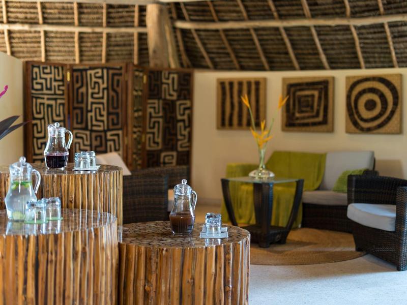 Espace lounge confortable avec meubles en bambou, vases en verre et coussins décoratifs dans un hôtel tropical.