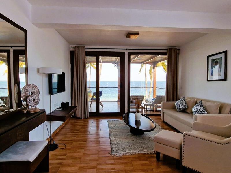 Helles Wohnzimmer mit großem Fenster, Sofa, Teppich, Klavier und Meerblick im Hintergrund.