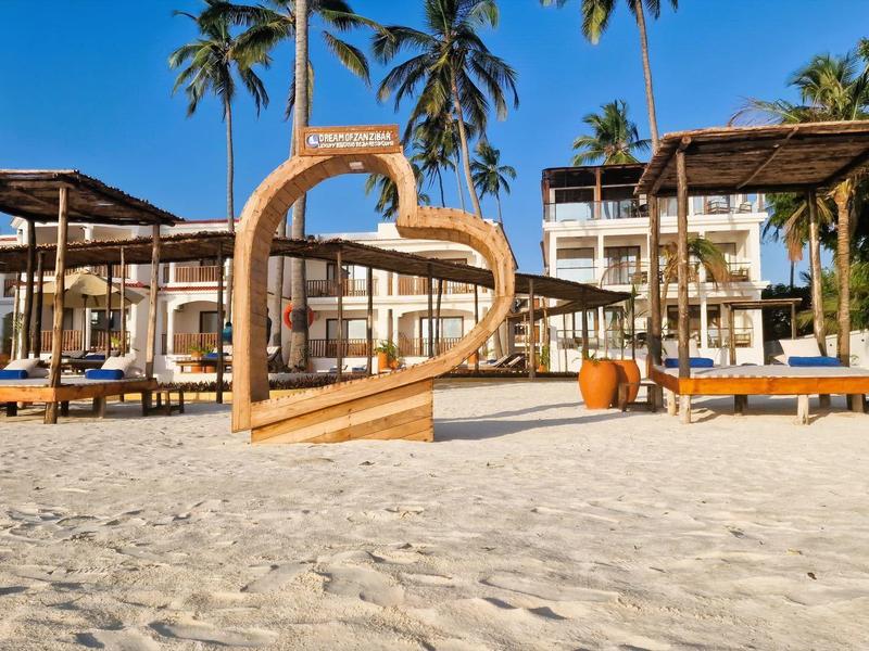 Strand mit Sand, Palmen, Sonnenliegen und einem großen Herzen aus Holz in der Mitte.