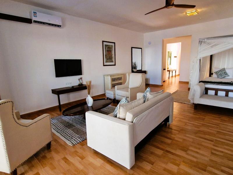 Modern eingerichtetes Wohnzimmer mit weißen Möbeln, Holzboden und Fernseher an der Wand.