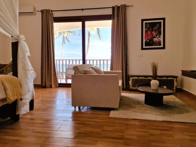 Helles Wohnzimmer mit Holzboden, Sofa, Teppich, Bett, Balkon und Meeresblick bei Sonnenlicht.