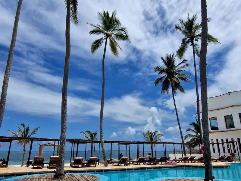 Blauer Pool mit Palmen und bewölktem Himmel, modernes Gebäude im Hintergrund.