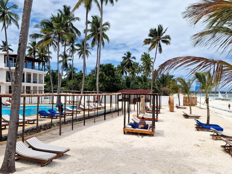 Strand mit Palmen, Liegen und Hängematten neben weißem Sand und blauem Meer bei bewölktem Himmel.