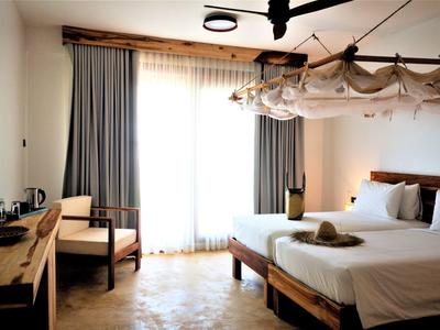 Helles Schlafzimmer mit Doppelbett, Holzstuhl, Schreibtisch und großen Vorhängen an der Fensterfront.