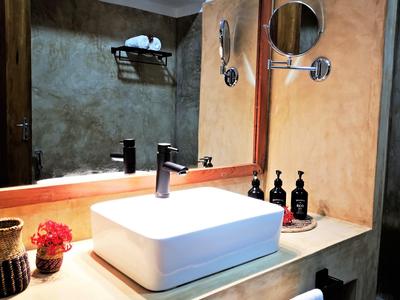 Badezimmer mit rechteckigem weißen Waschbecken, schwarzem Wasserhahn und dekorativen Flaschen auf dem Holz.