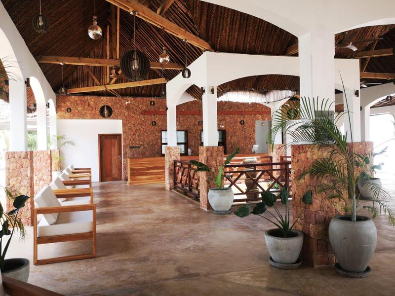 Helles Restaurant mit Holzdach, weißen Bögen, Holztischen, Stühlen und grünen Pflanzen in Töpfen.