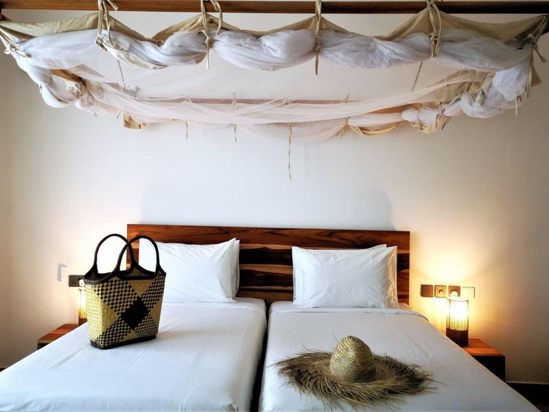 Modernes Schlafzimmer mit weißen Kissen, Holzbett, Strohhut auf Decke und Tasche am Bettrand.