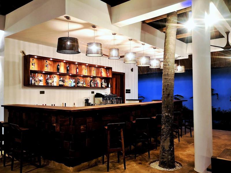 Moderne Bar mit Holztheke, dunklen Barhockern und kräftiger Beleuchtung innen und außen.