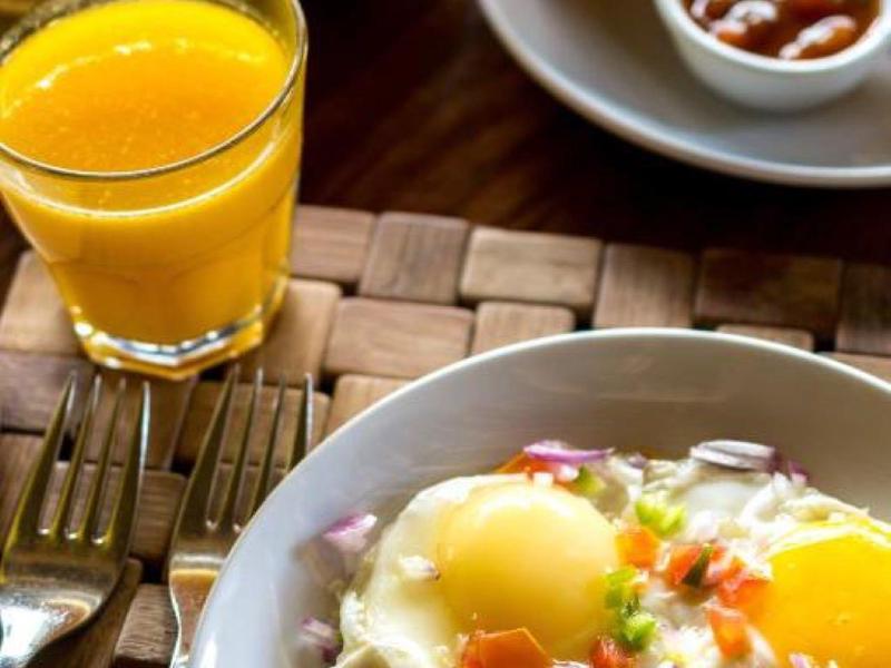 Frühstück mit Spiegeleiern, Gemüse, frisch gepresstem Orangensaft, Waffeln und Früchten.