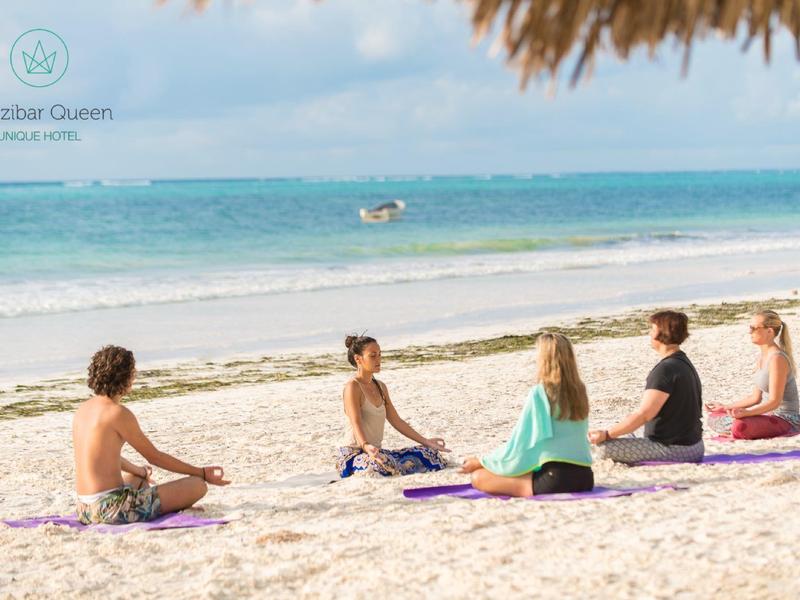 Vier Korbstühle mit roten Kissen stehen auf Terrasse mit Blick auf weißen Sandstrand und blaues Meer.