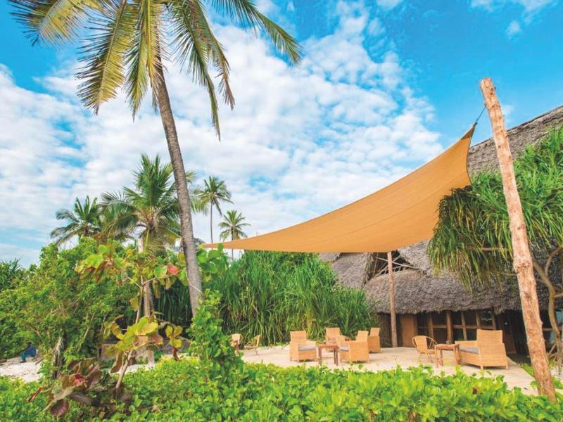 Strandrestaurant mit Palmendach, Sonnensegel und tropischer Vegetation unter blauem Himmel.