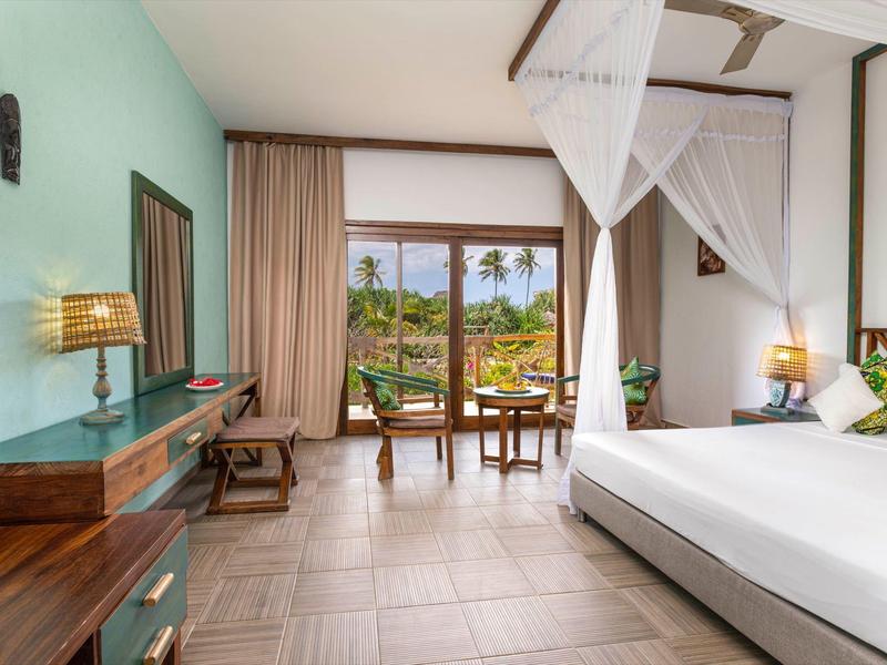 Helles, geräumiges Zimmer mit Doppelbett, Moskitonetz, Holzmöbeln und Blick auf tropischen Garten.