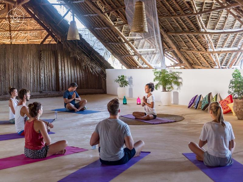Helles Schlafzimmer mit Himmelbett, Holzbalken, Blick auf Terrasse und Palmenlandschaft draußen.