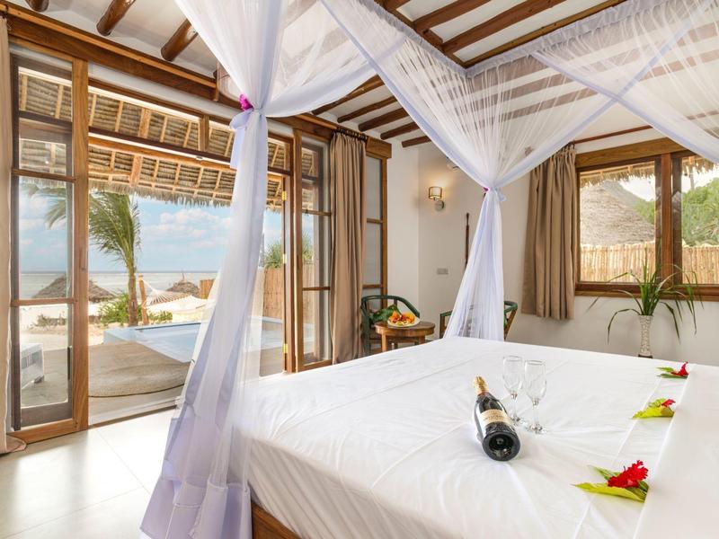 Helles Schlafzimmer mit Himmelbett, offenem Fenster, Meerblick und Flasche Wein auf weißer Bettdecke.