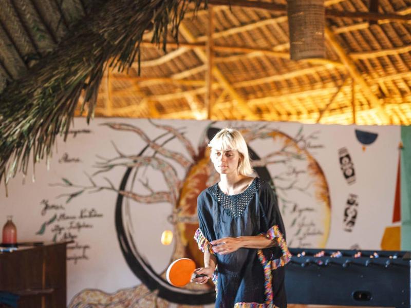 Eine Frau spielt Tischtennis in einem Raum mit Bambusdecke und natürlicher Dekoration.