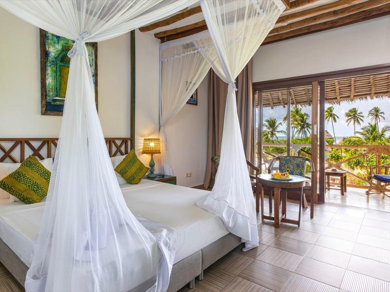 Helles Schlafzimmer mit Himmelbett und Moskitonetz, Zugang zu Balkon mit Blick auf Palmen und Meer.