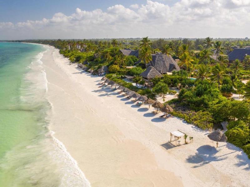 Weißer Sandstrand mit Palmen, Sonnenschirmen und klarem, türkisfarbenem Meer unter blauem Himmel.