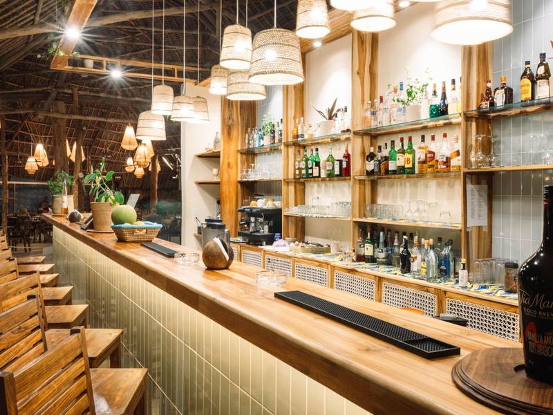 Moderne Bar mit langen Holzstühlen, hängenden Lampen und Regalen voller Flaschen.