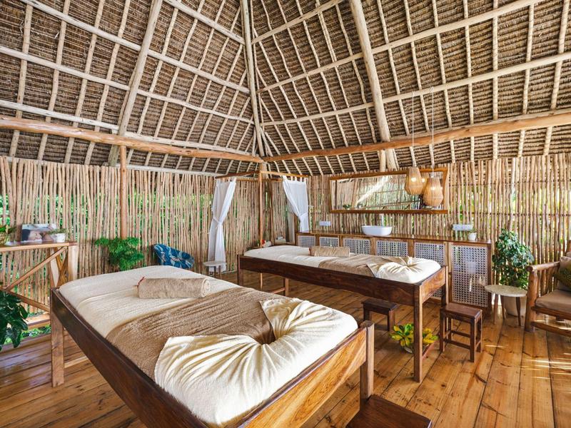 Innenraum einer Holzhütte mit traditionellen Bambuswänden, Strohdach und zwei Massagebetten.