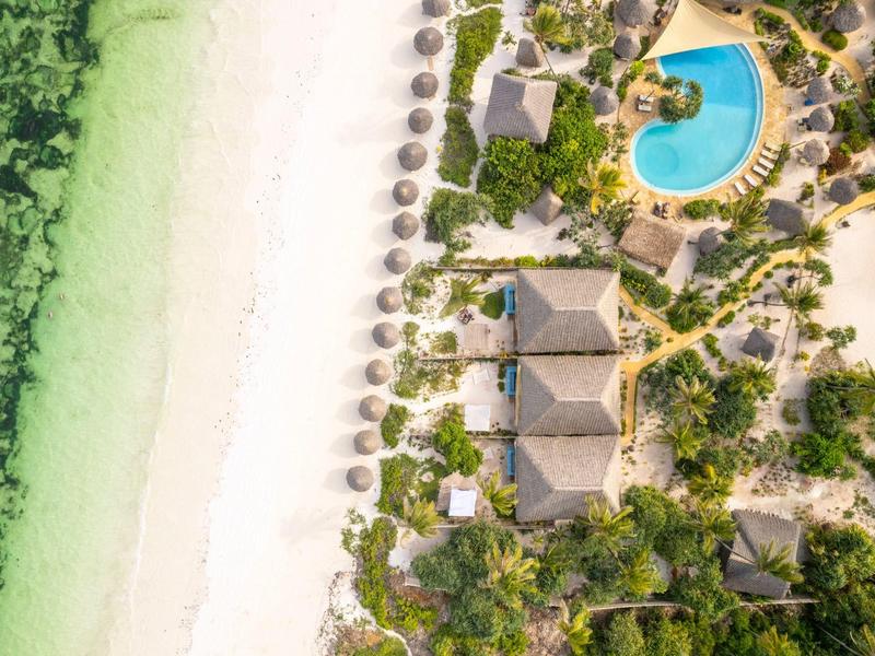 Strand mit weißem Sand, türkisfarbenem Wasser, Palmen, Bungalows und rundem Pool aus der Vogelperspektive.