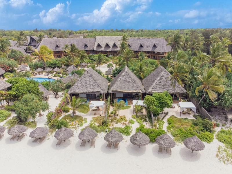 Tropischer Strand mit Palmen, Strohdächern und einem Resort am Meer unter blauem Himmel.