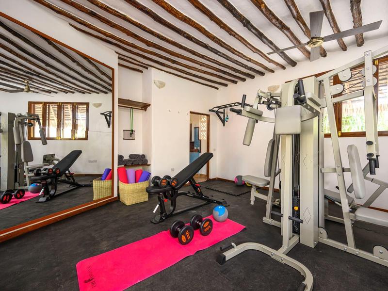 Kleines Fitnesszimmer mit schwarzen Geräten, rosa Matte und Holzdeckenbalken.