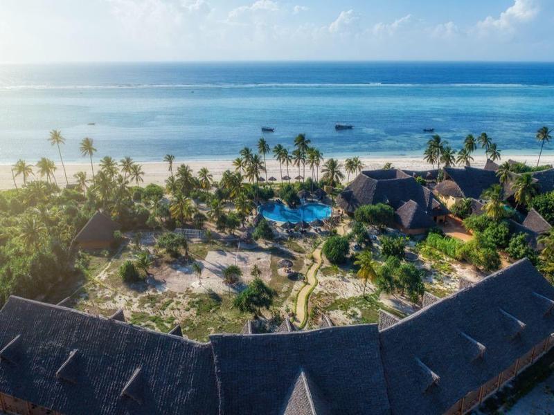 Strandresort mit Palmen, Sandstrand und blauer Lagune unter hellem Himmel bei Sonnenlicht.