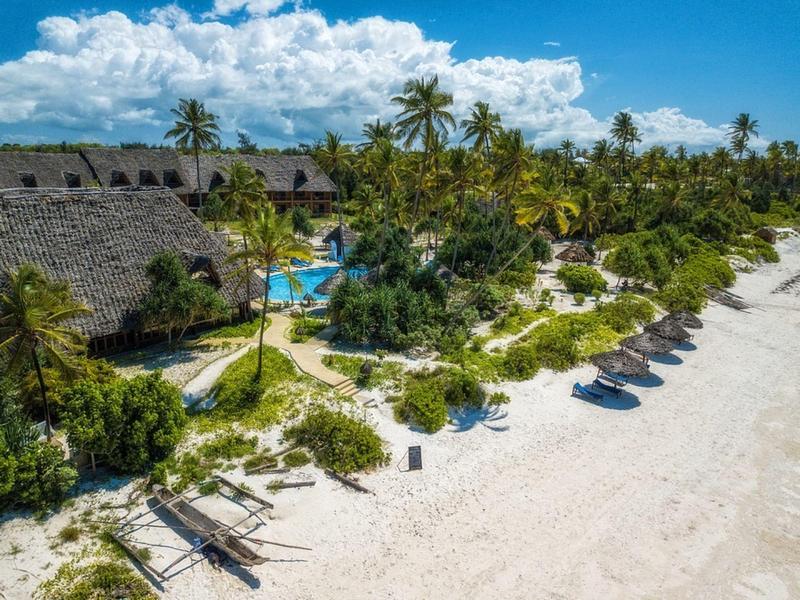 Strand mit weißen Sand, Palmen und Strohdachbungalows neben türkisblauem Wasser unter blauem Himmel.