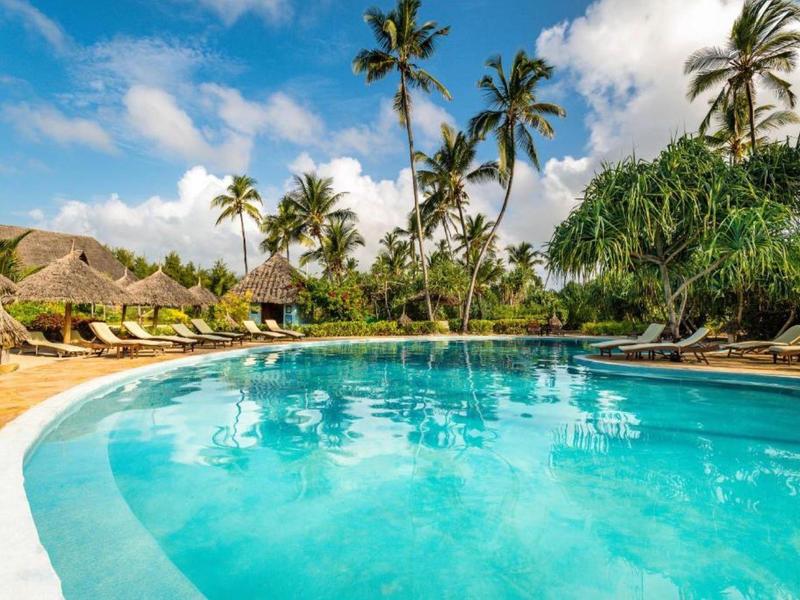 Runder Pool mit blauem Wasser, Palmen und Liegestühlen unter blauem Himmel mit Wolken.