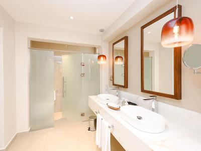 Nowoczesna łazienka hotelowa z dwoma umywalkami i szklaną kabiną prysznicową.