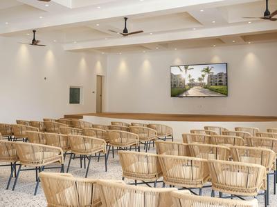 Nowoczesna sala konferencyjna z krzesłami z wikliny i dużym obrazem na ścianie.
