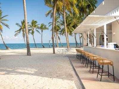 Bar na świeżym powietrzu z stołkami i palmami na słonecznej plaży.