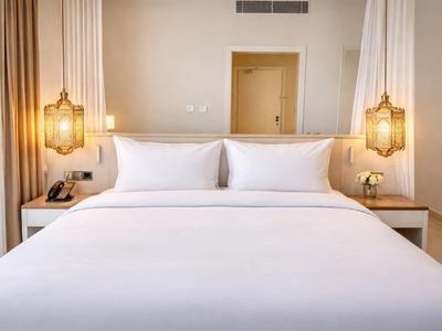 Jasny pokój hotelowy z dużym łóżkiem podwójnym i ciepłymi wiszącymi lampami.