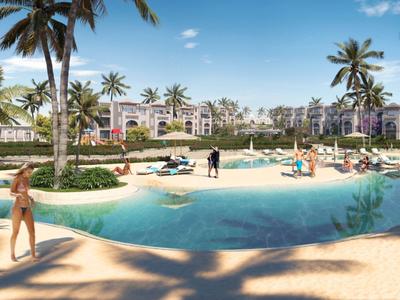 Large hotel pool with palm trees and lounge chairs in front of a multi-story resort building under a blue sky.