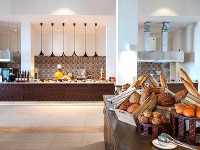 Nowoczesne bufet hotelowy z różnymi rodzajami pieczywa i otwartą kuchnią w tle.