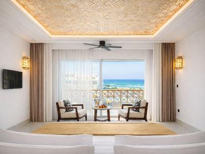 Jasny pokój hotelowy z widokiem na morze, dwoma krzesłami przy oknie i przytulną atmosferą.