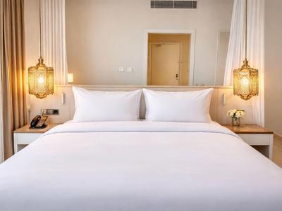 Jasno urządzone pokoje hotelowe z dużym łóżkiem, białymi poduszkami i dwoma złotymi lampami wiszącymi.