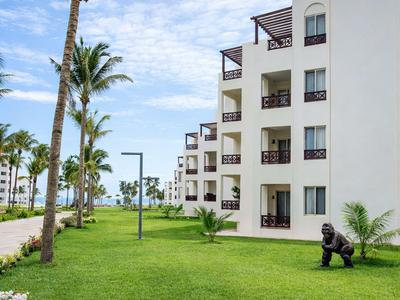 Widok nowoczesnego budynku hotelowego z balkonami obok zadbanego trawnika i palm.