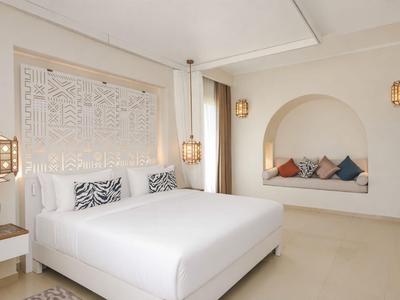 Jasna, nowoczesna sypialnia z dużym łóżkiem, ozdobnym zagłówkiem i przytulną wnęką z poduszkami.