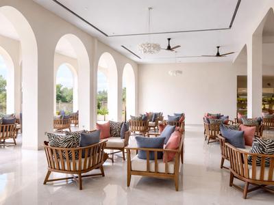 Jasny salon hotelowy z okrągłymi drewnianymi meblami, poduszkami i dużymi łukami z widokiem na zewnątrz.