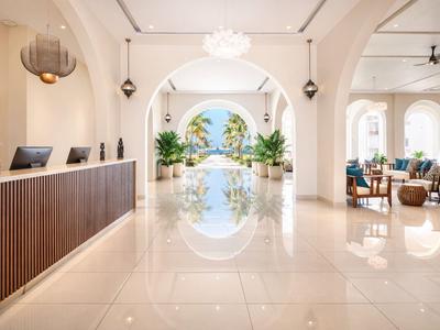 Jasna lobby hotelowa z recepcją, roślinami i częścią wypoczynkową z łukowatymi sufitami.