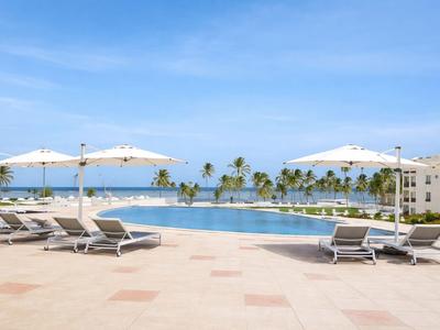 Basen typu infinity z leżakami, parasolami i widokiem na morze z palmami.