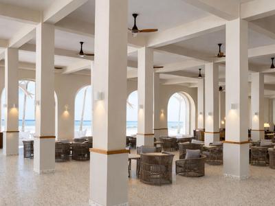 Przestronna, jasna część wypoczynkowa hotelu z miejscami do siedzenia i dużymi oknami z widokiem na morze.