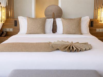 Nowoczesne łóżko podwójne z białą pościelą, beżowymi poduszkami i dekoracyjnie złożonym ręcznikiem.