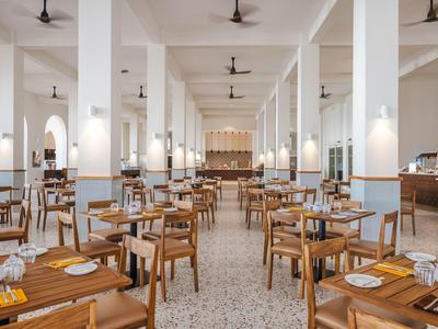 Jasna, przestronna restauracja z drewnianymi krzesłami i stołami ustawionymi w równych rzędach.