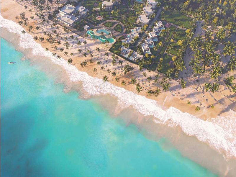 Widok z powietrza na ośrodek nad piaszczystą plażą z turkusowym morzem i zielonymi drzewami