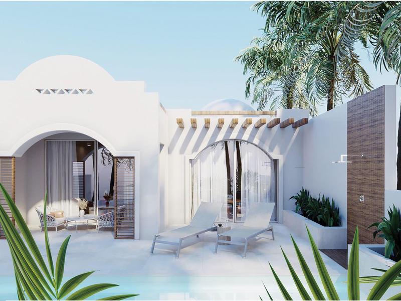 Biały budynek z oknami w kształcie łuku, taras z leżakami i palmami na pierwszym planie.